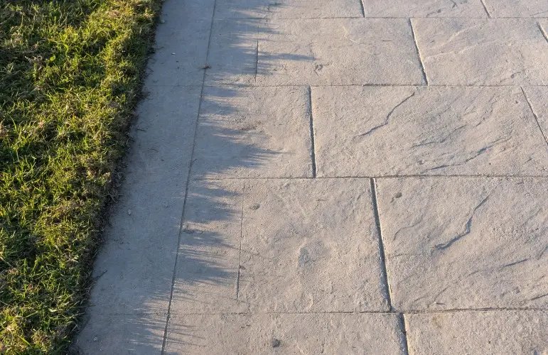Acera de hormigón impreso imitación losa de piedra bordeando el césped de una urbanización en Huelva