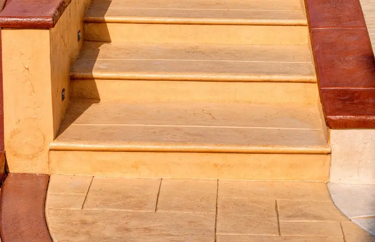 Escalera exterior y coronación de piscina de hormigón impreso color arena con canto redondeado antideslizante en Huelva