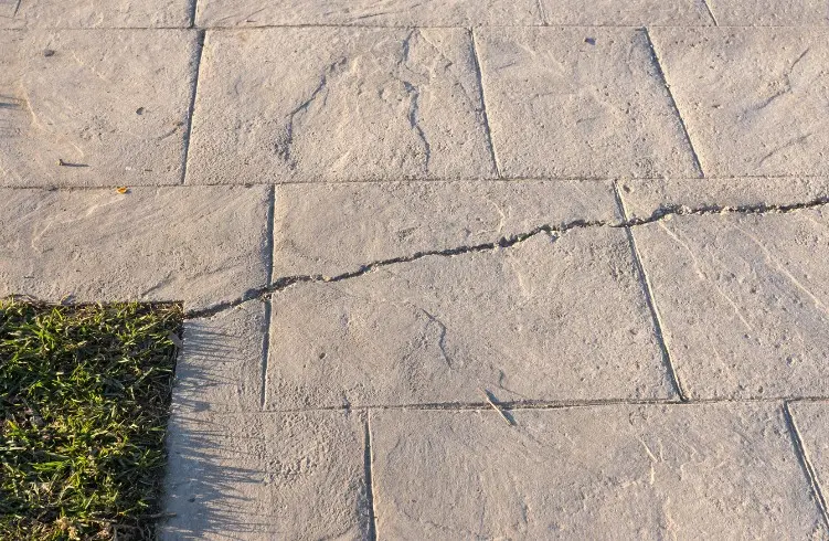 Fisura en la junta de un pavimento de hormigón impreso imitación losa de piedra en un jardín de Huelva
